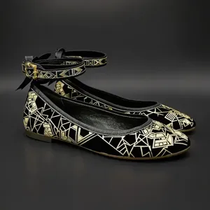 Pair of black ballet flats with gold geometric patterns and ankle straps on a dark background