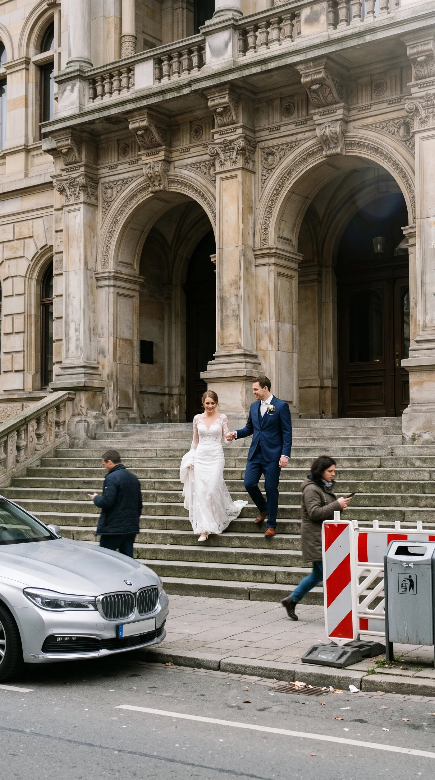 Before: a bride and groom walking down town hall steps with a parked car, two people on their phones, a construction barrier and a bin around them, used as a background cleanup example on getimg.ai
