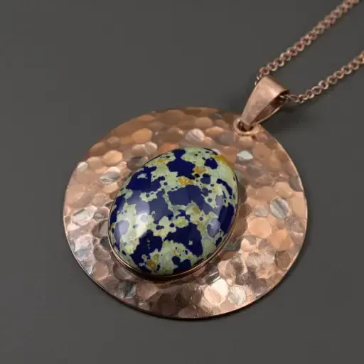 Hammered copper-colored pendant with a blue and cream oval stone on a chain