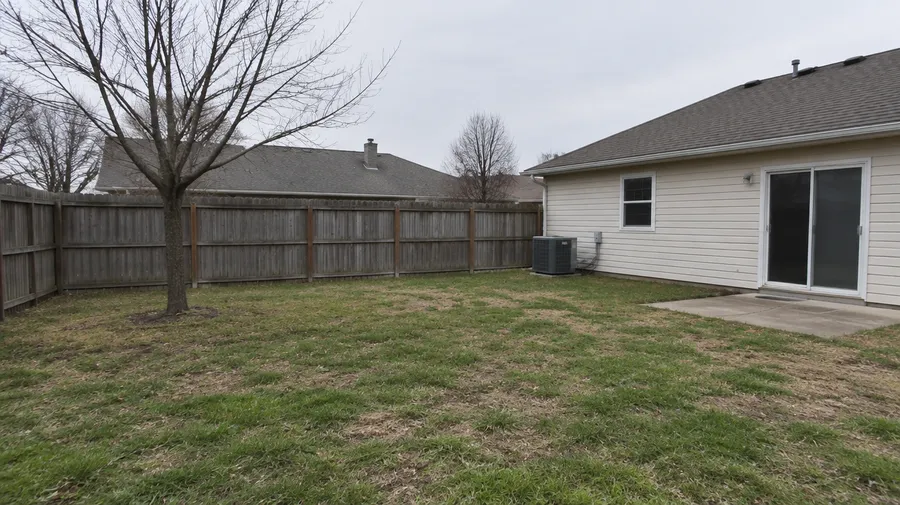 Suburban backyard before redesign, with a patchy lawn, wooden fence and concrete slab