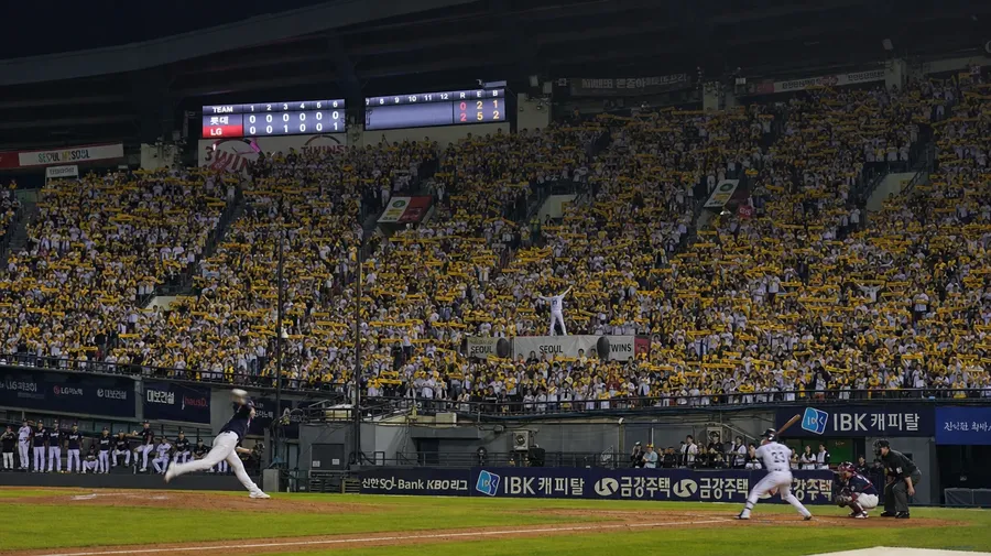 KBO night game in Seoul with synchronized crowd choreography and team-color towels, AI-generated stock baseball image.