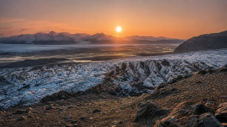 Pale-gold disc of the midnight sun low above an Icelandic glacial plain and ridge, AI sun stock photo.