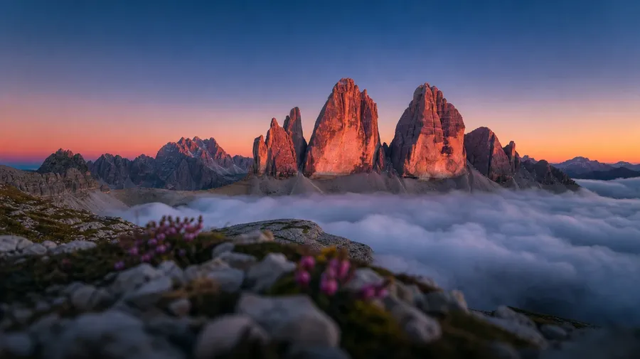 Dolomite peaks at alpenglow with valley fog below at sunrise, AI stock sunrise picture.
