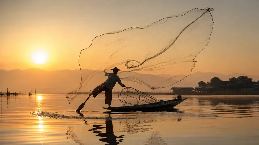 Burmese fisherman casting a circular net on Inle Lake at dawn, AI stock sunrise picture.