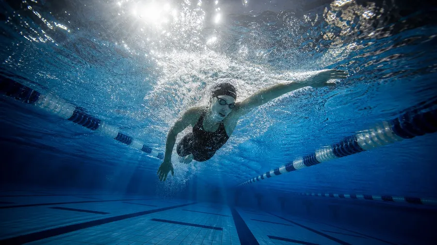Underwater wide of a female swimmer mid-freestyle stroke with caustic light beams, AI-generated swimming images.