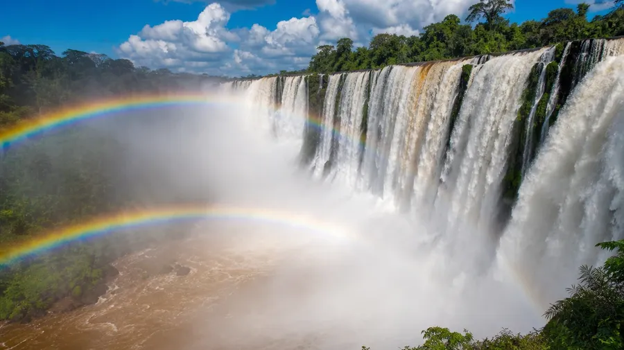 AI-generated Iguazu jungle plunge thundering into a roiling pool with mist and a vivid rainbow in the spray.