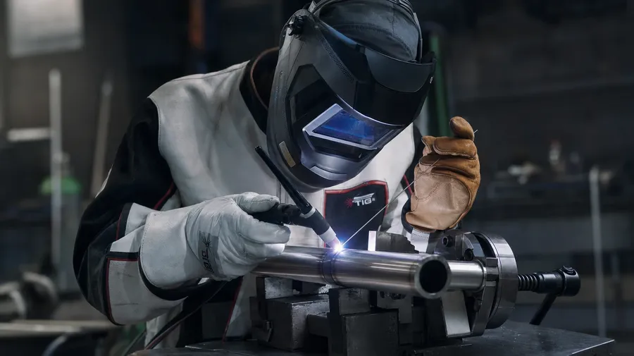 AI stock welding image of a TIG welder running a tight tungsten arc on stainless tubing in a dim fab shop.