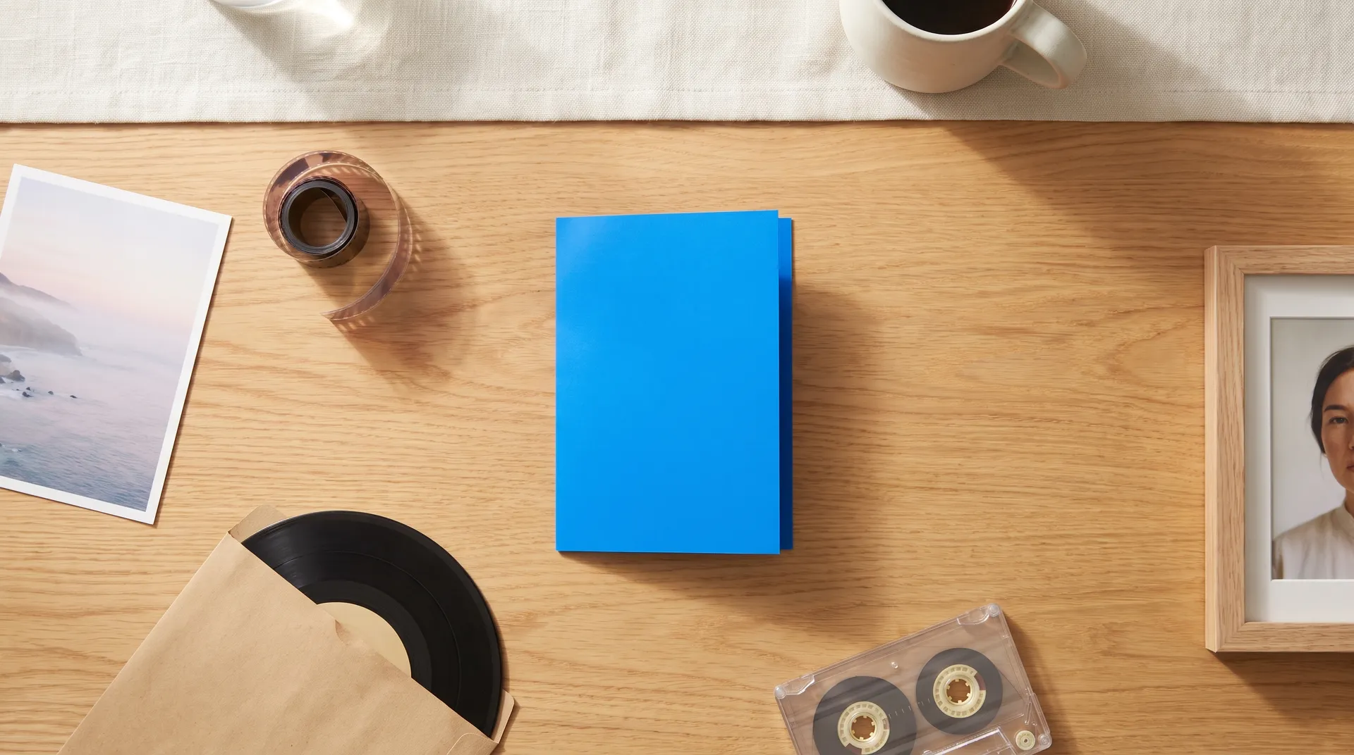 Blue folded card on an oak table surrounded by a coastal photo print, a film coil, a vinyl record, a cassette, and a framed portrait, featured image for the getimg.ai plugin in ChatGPT, generated on getimg.ai