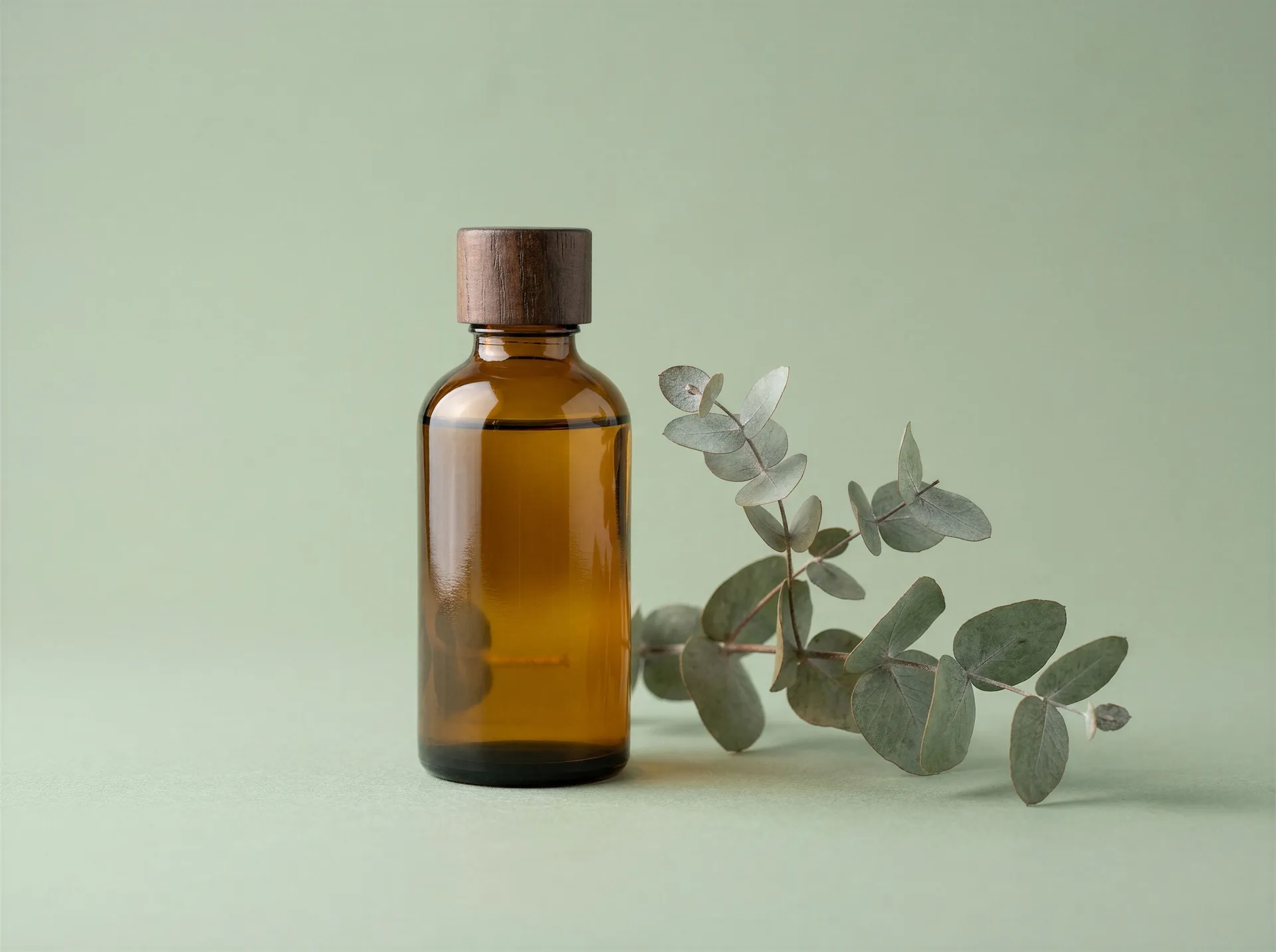 An amber glass dropper bottle beside a sprig of dried eucalyptus on a sage green backdrop, cropped tighter than the hero shot. Step three of a team campaign, where marketing generates channel variants from the chosen concept. Image generated with getimg.ai.