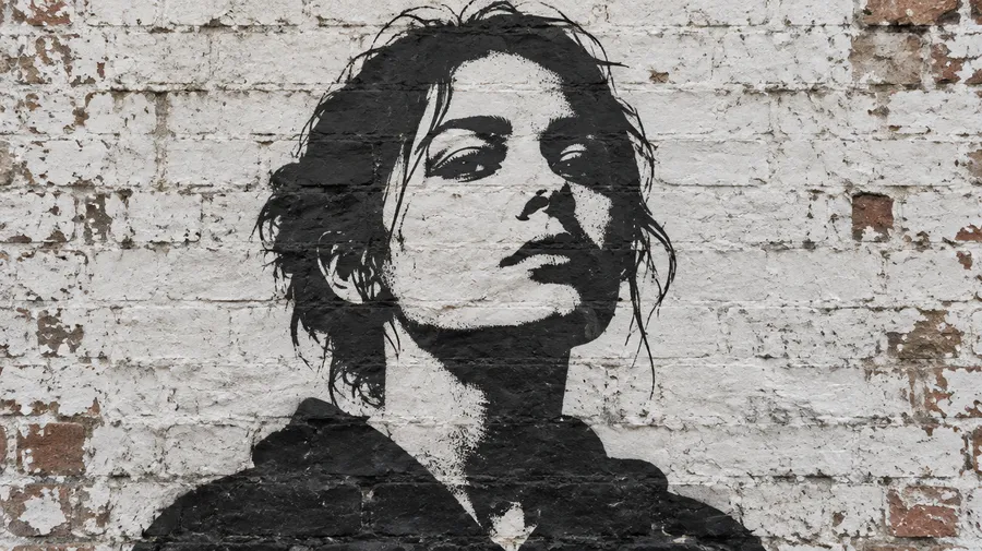Black stencil street art portrait sprayed on a weathered white brick wall