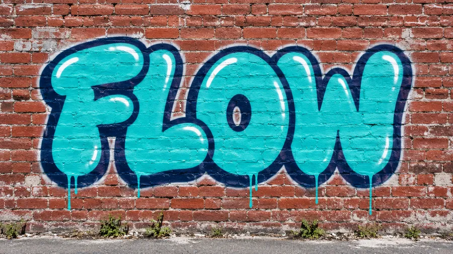 Bubble-letter graffiti spelling FLOW in turquoise on a red brick wall