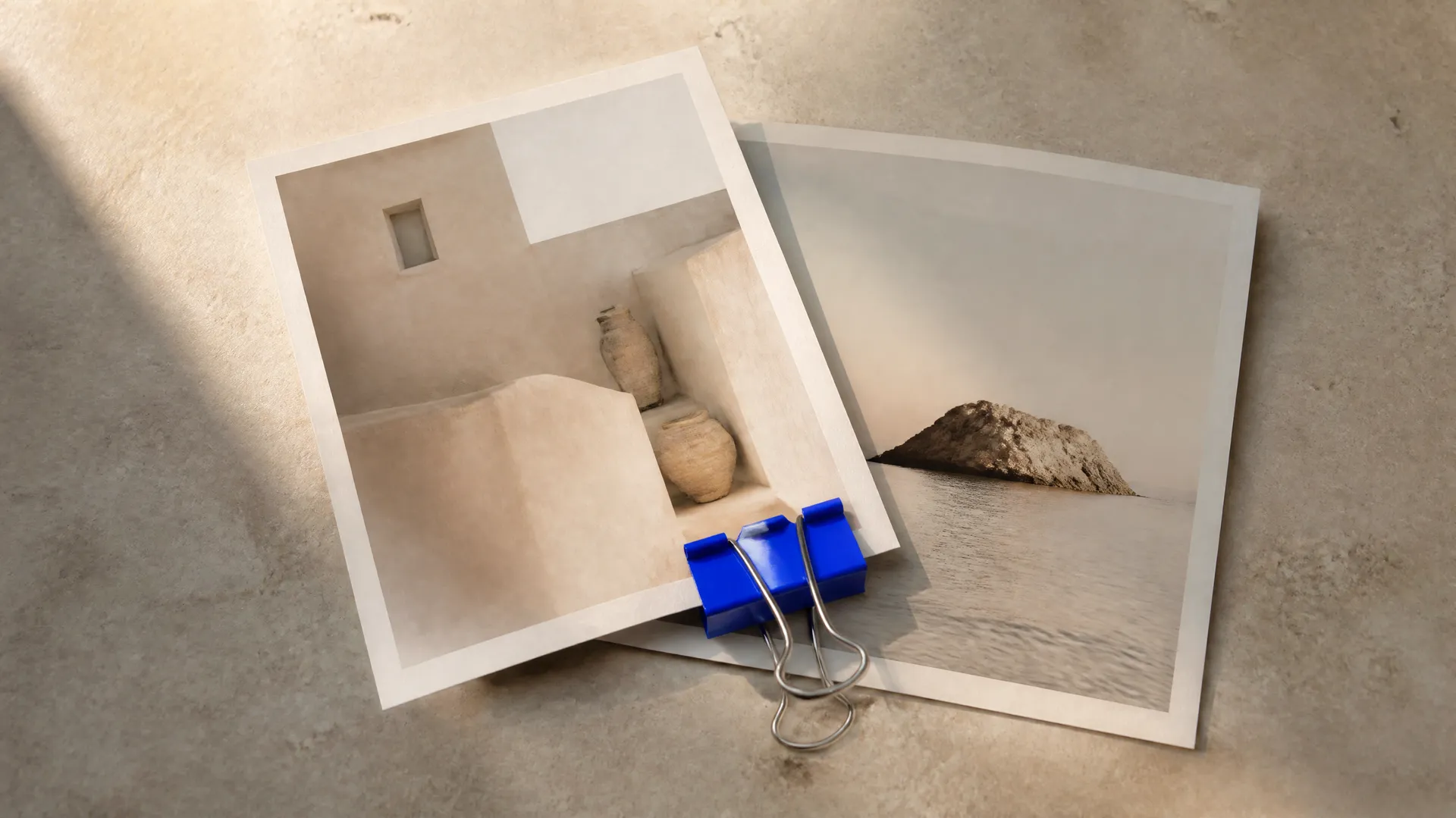 Two overlapping matte photo prints on a warm stone surface joined by an electric-blue binder clip, representing AI image-transition video between two images. Generated with getimg.ai.