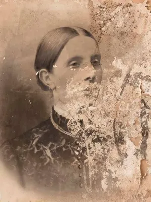 A heavily faded and water-stained sepia studio portrait of a woman with centre-parted hair, cracked and blotched with age: the damaged original before AI restoration on getimg.ai.