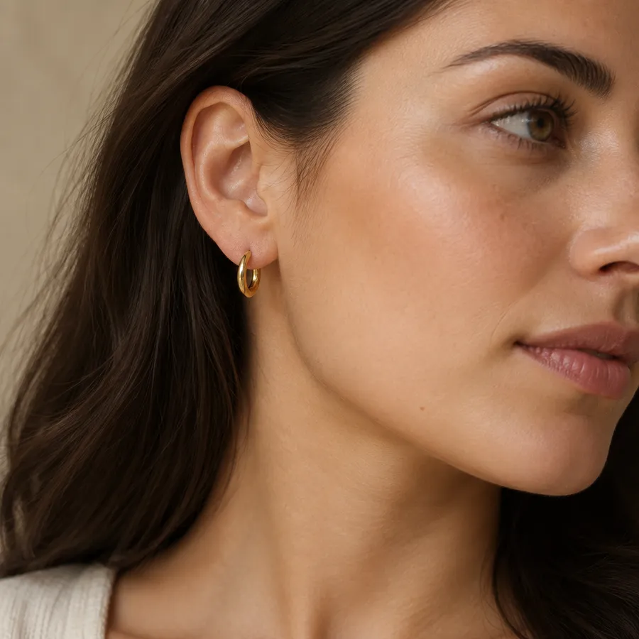 Close crop of a woman's ear and jawline in profile wearing a small gold hoop earring, hair tucked back.