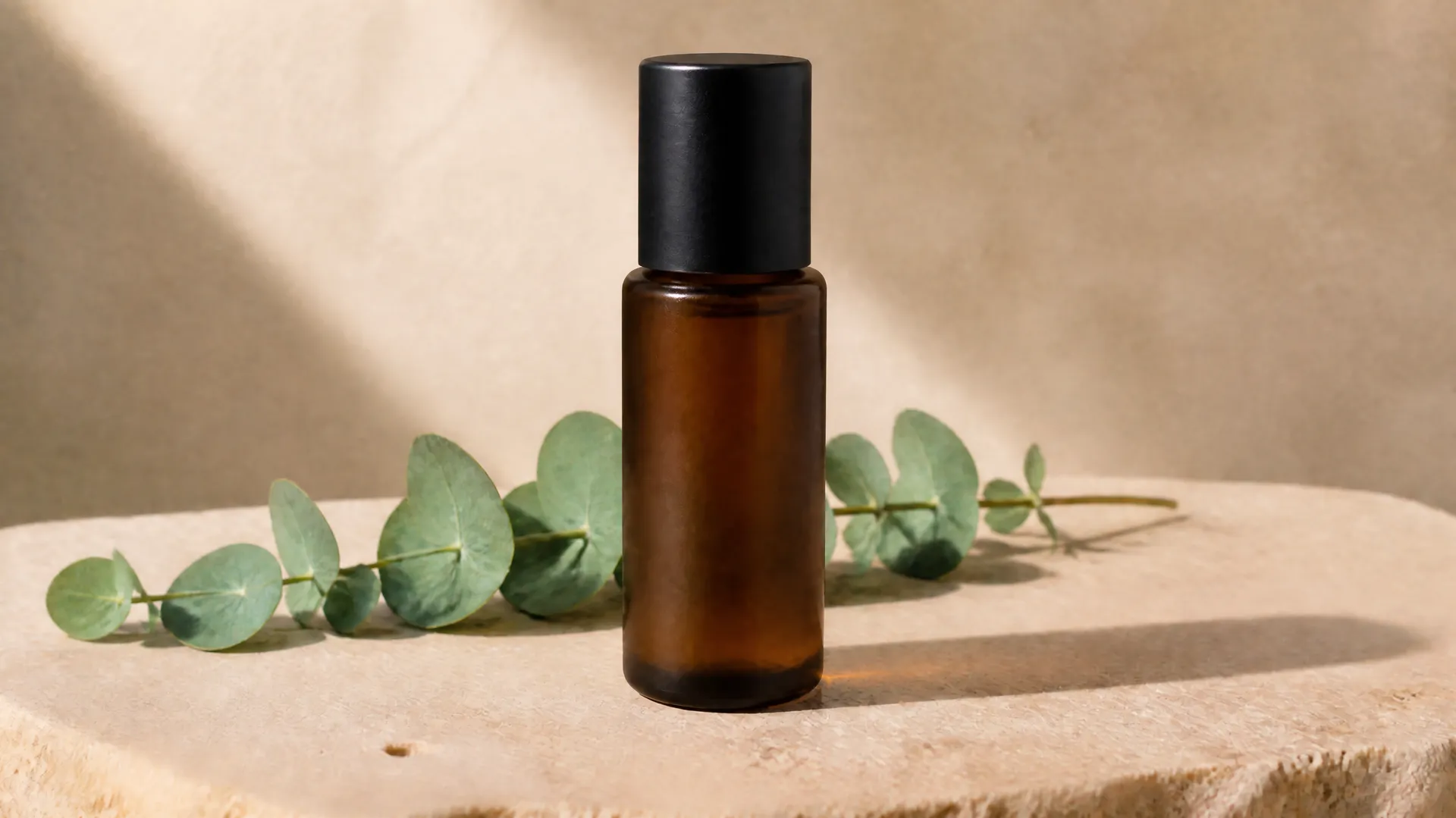 Amber bottle with a black cap beside eucalyptus leaves on a sunlit stone slab.