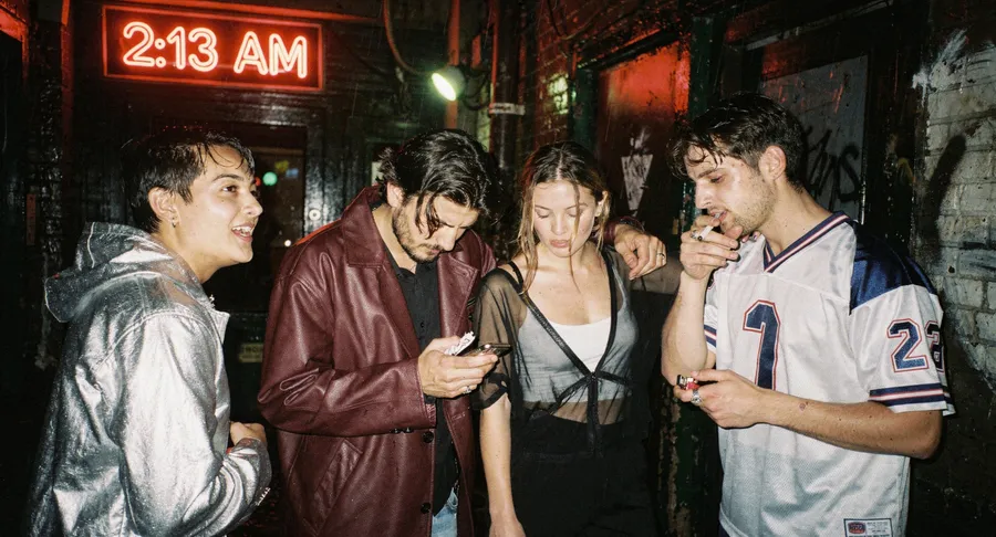 Flash night photo of four friends leaving a club under a red 2:13 AM neon sign in a rain-soaked alley, generated on getimg.ai with FLUX.2 [max] for an AI image realism test.