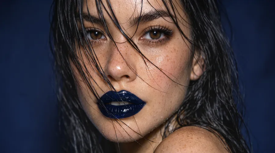 Extreme macro beauty portrait of a young woman with wet dark hair across her face, glossy dark-blue lips and freckled skin under hard flash, generated on getimg.ai with GPT Image 1.5 for an AI image realism test.