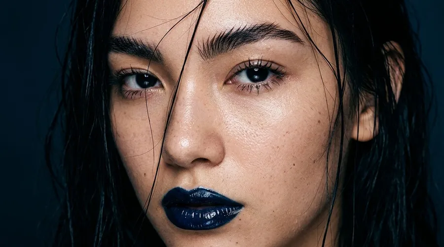 Extreme macro beauty portrait of a young woman with wet dark hair across her face, glossy dark-blue lips and freckled skin under hard flash, generated on getimg.ai with Nano Banana 2 for an AI image realism test.