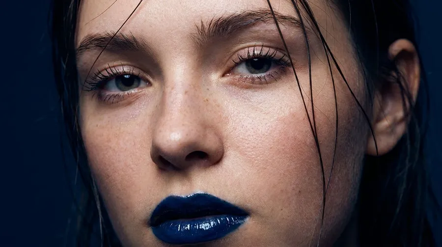 Extreme macro beauty portrait of a young woman with wet dark hair across her face, glossy dark-blue lips and freckled skin under hard flash, generated on getimg.ai with Nano Banana Pro for an AI image realism test.