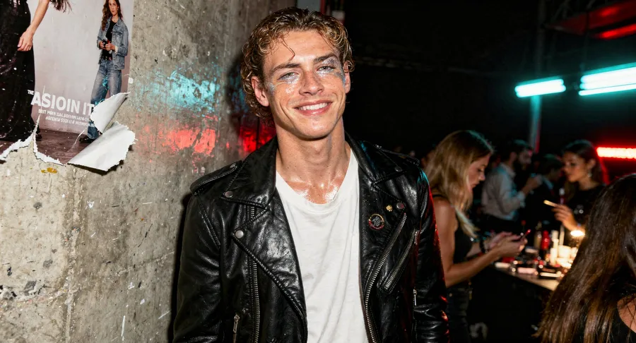 Backstage fashion-show photo recreating the reference man in a leather jacket with wet-look hair, testing identity preservation, generated on getimg.ai with FLUX.2 [max] for an AI image realism test.