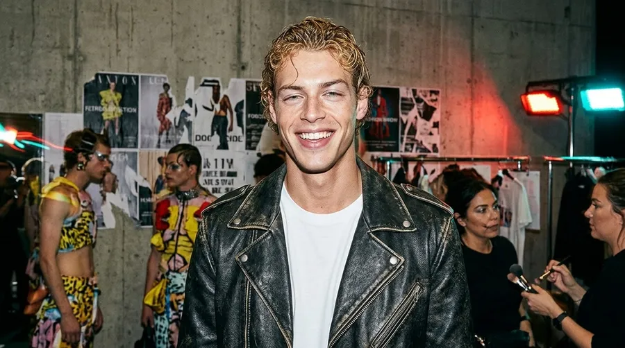 Backstage fashion-show photo recreating the reference man in a leather jacket with wet-look hair, testing identity preservation, generated on getimg.ai with Nano Banana 2 for an AI image realism test.