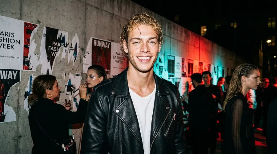 Backstage fashion-show photo recreating the reference man in a leather jacket with wet-look hair, testing identity preservation, generated on getimg.ai with Nano Banana Pro for an AI image realism test.