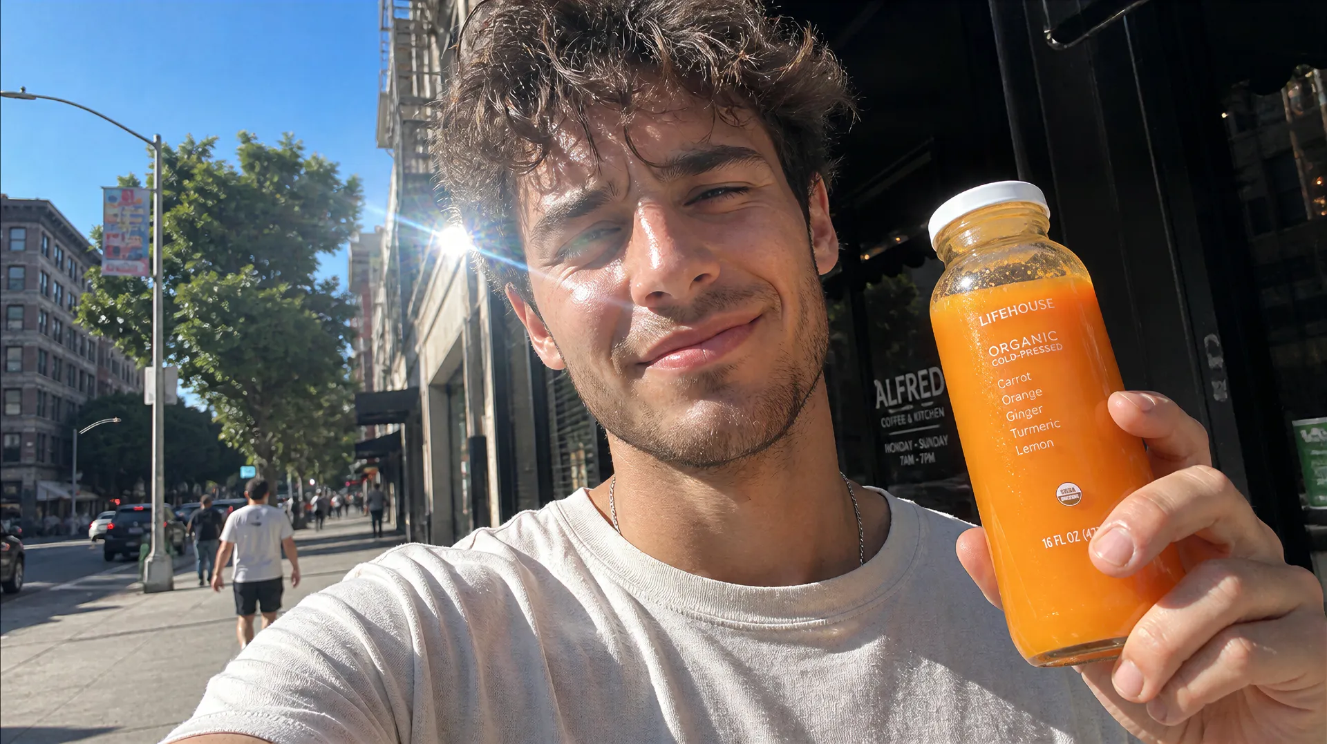 a selfie-style photo of a young man holding an organic juice bottle on a city street, slightly harsh midday light, minor lens flare, phone-camera look with natural grain, casual imperfect framing, generated on getimg.ai
