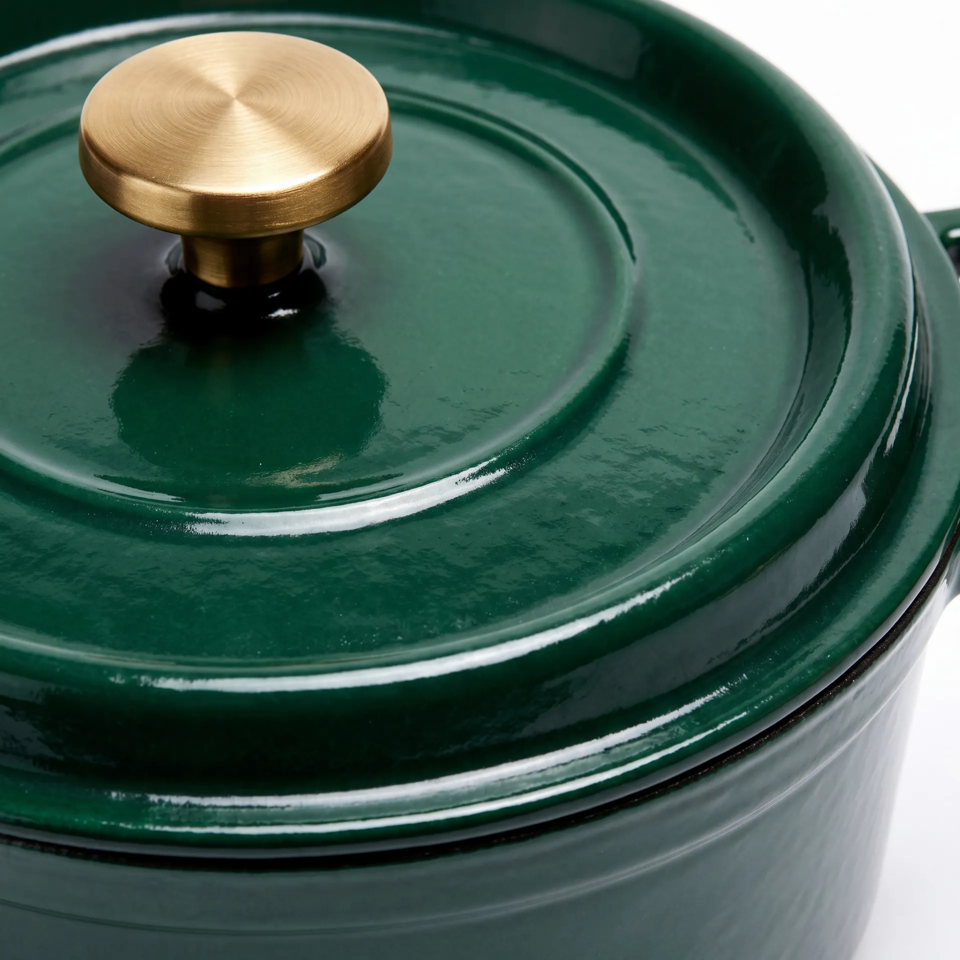 Sharp close-up of the brushed brass knob and glossy green enamel lid rim of the cast iron casserole pot, showing the brass grain and the clean lid edge in crisp focus. Detail crop generated in getimg.ai.