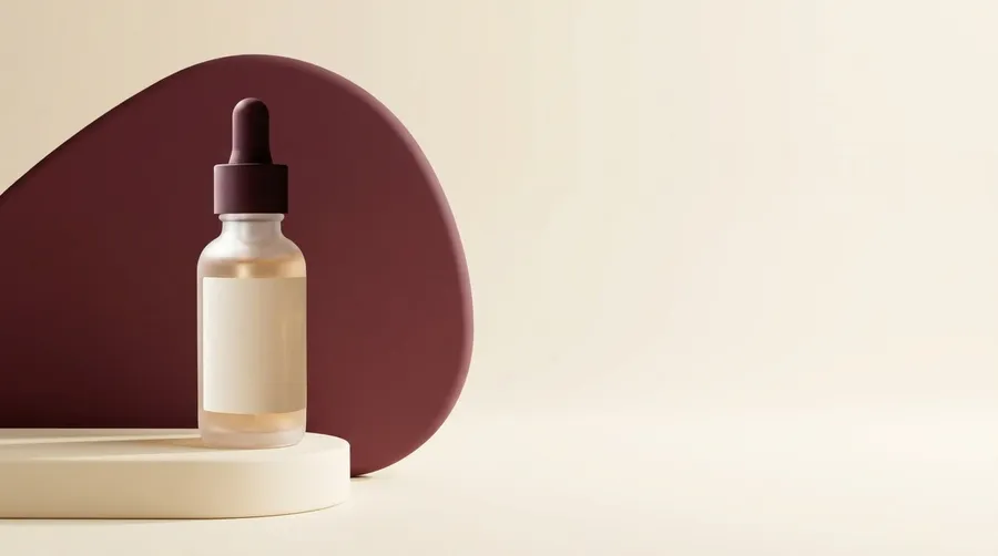 Frosted glass serum bottle with a matte burgundy dropper cap standing on a cream pedestal in front of a soft burgundy shape, with wide empty cream space on the right for headline copy. Email hero creative for a skincare launch campaign, generated with AI on getimg.ai.