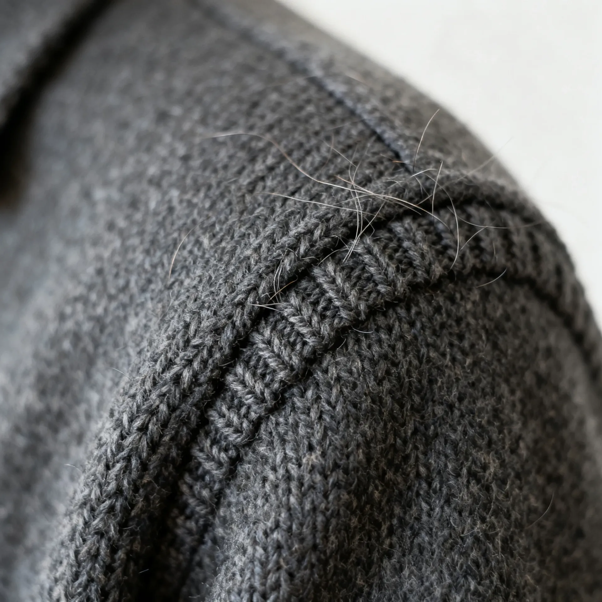Macro detail of a charcoal knitted wool shoulder seam with individual fibres and stray hairs in sharp focus. Example of the detail photographers check after upscaling on getimg.ai, generated with getimg.ai.