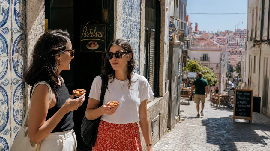AI stock street photography of two friends sharing a pastel de nata on a tiled Lisbon side street at midday