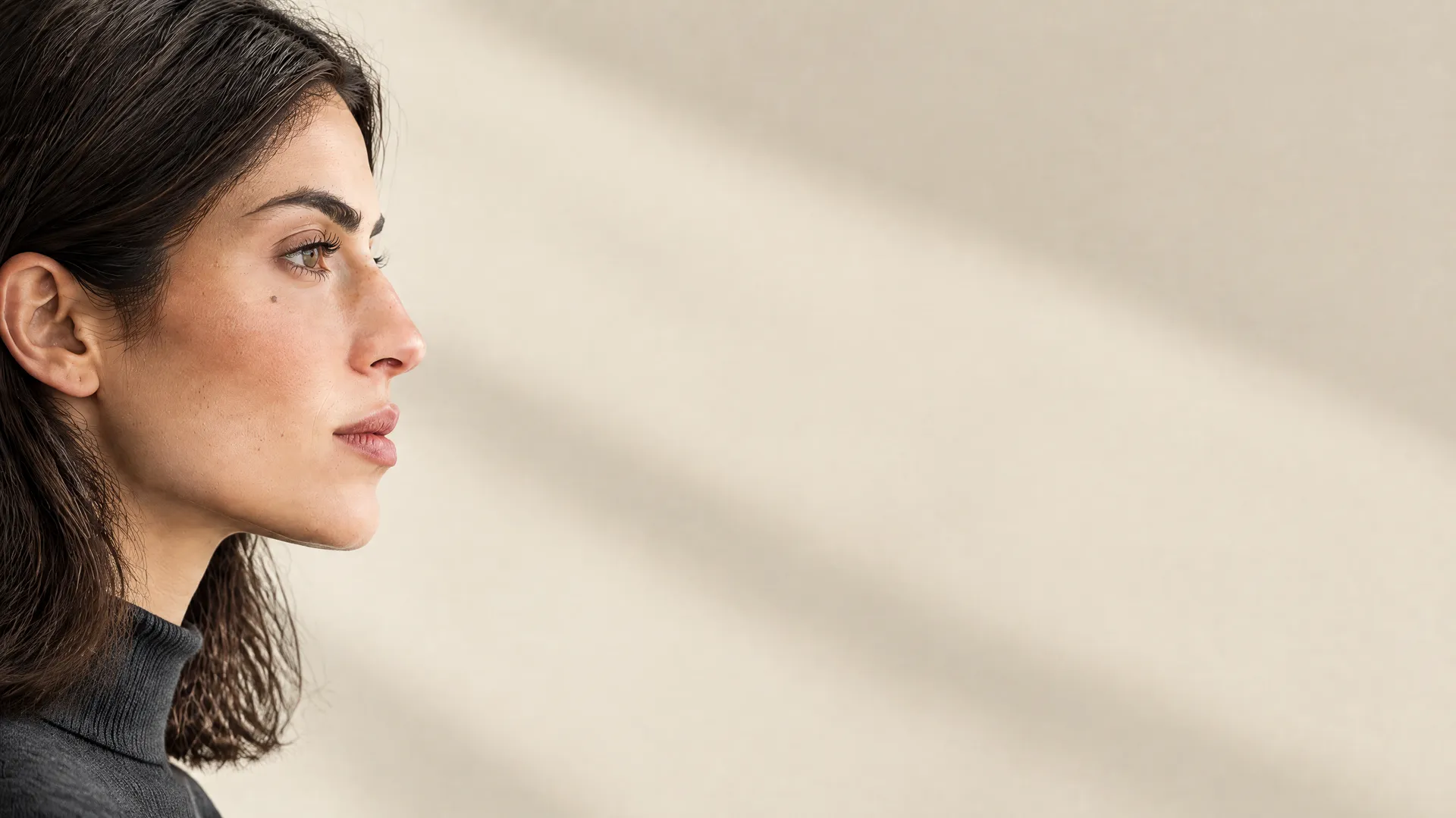 An AI-generated near-profile portrait of Mara in a graphite high-neck top against a cream wall, a Round 5 chaos-mode angle test; created on getimg.ai.