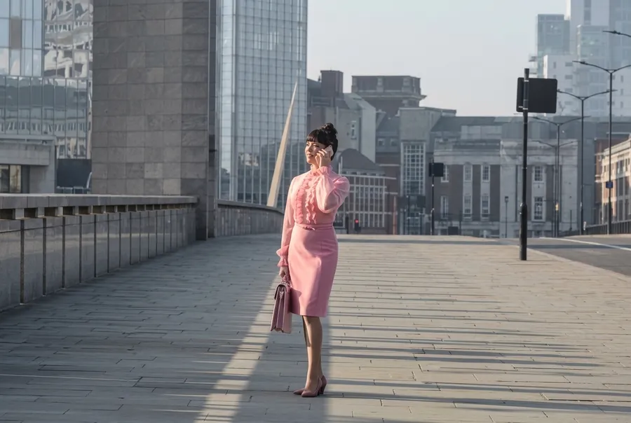 After removing objects from the photo with AI on getimg.ai: the same woman in a pink dress on the phone, now alone on the empty city bridge with all the surrounding commuters erased and the paving and skyline cleanly rebuilt behind her.
